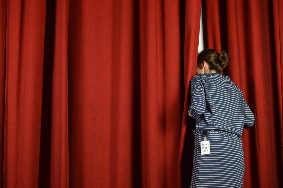 Woman with a backstage pass looking behind the red curtains on a stage