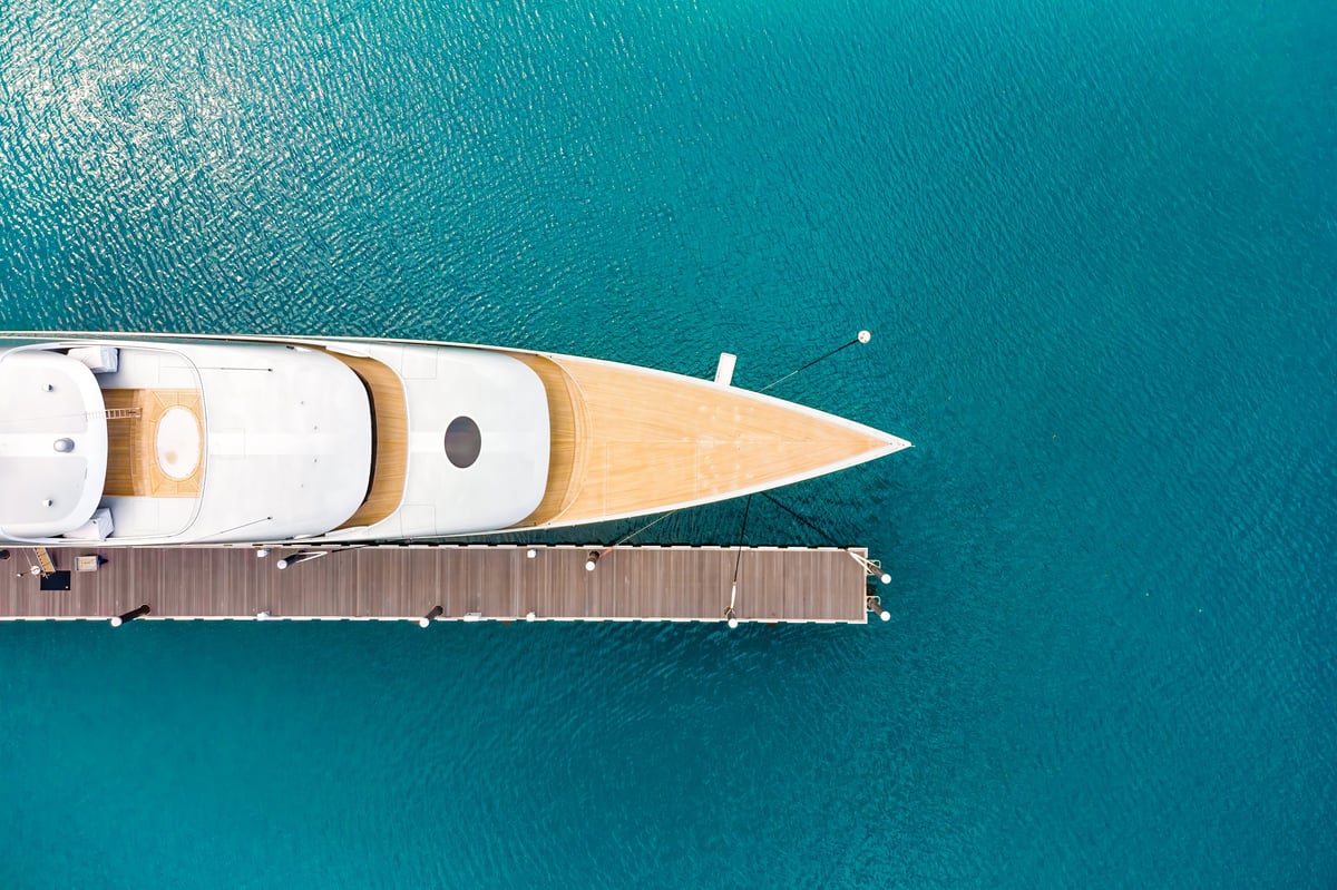 Luxurious modern expensive yacht moored to a long pier in a bay with crystal clear turquoise ocean water