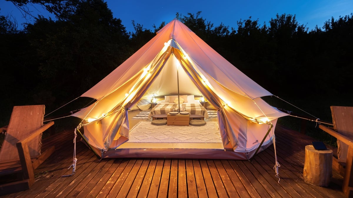 Luxury glamping tent interior with lamps and wooden chairs at night