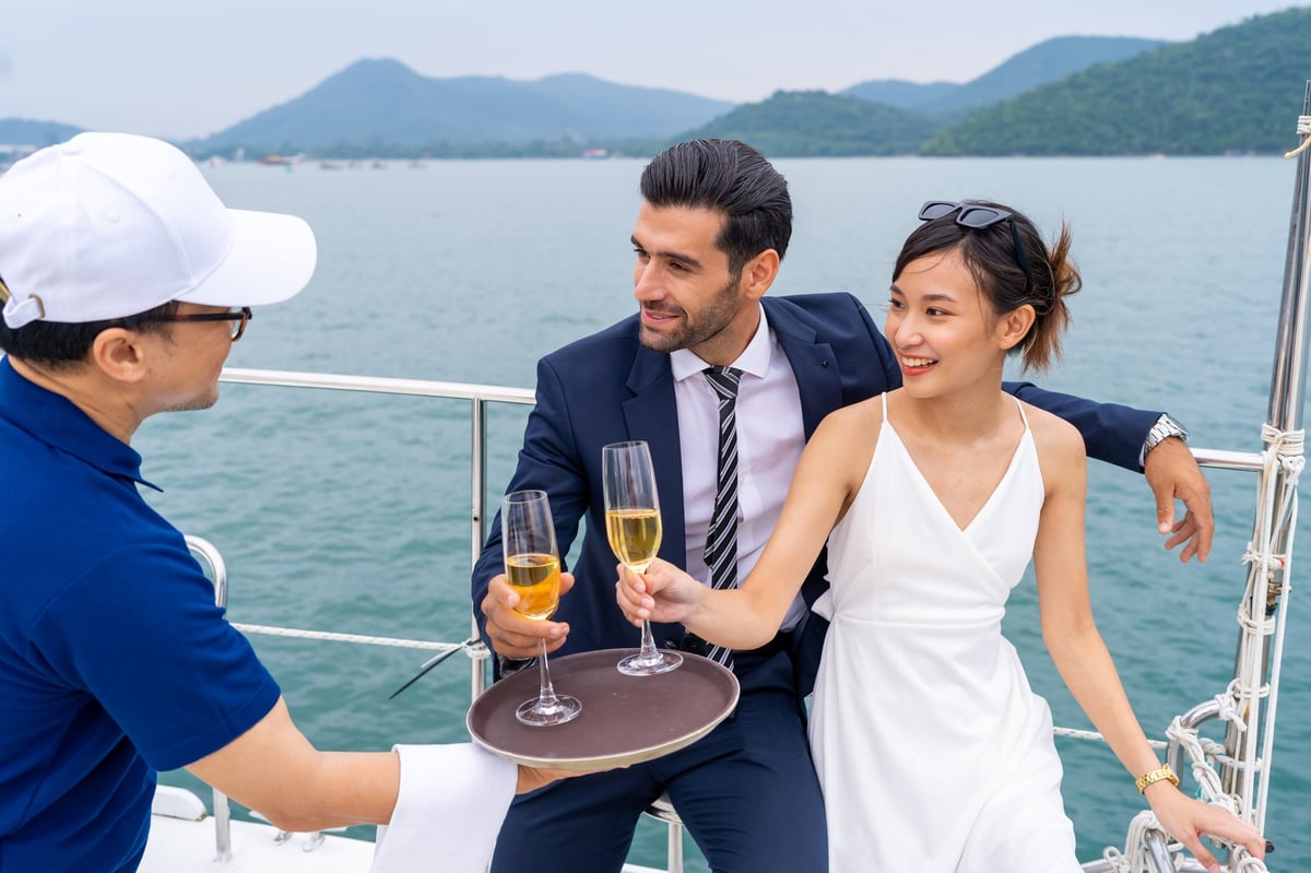 Waiter serving champagne to passenger tourist while luxury private catamaran boat yacht sailing in the ocean