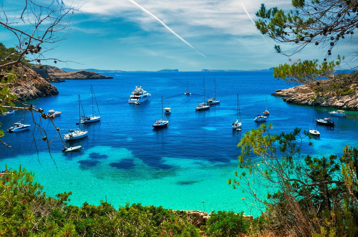 A sailboat and a yacht anchored at a turquoise Caribbean lagoon cove