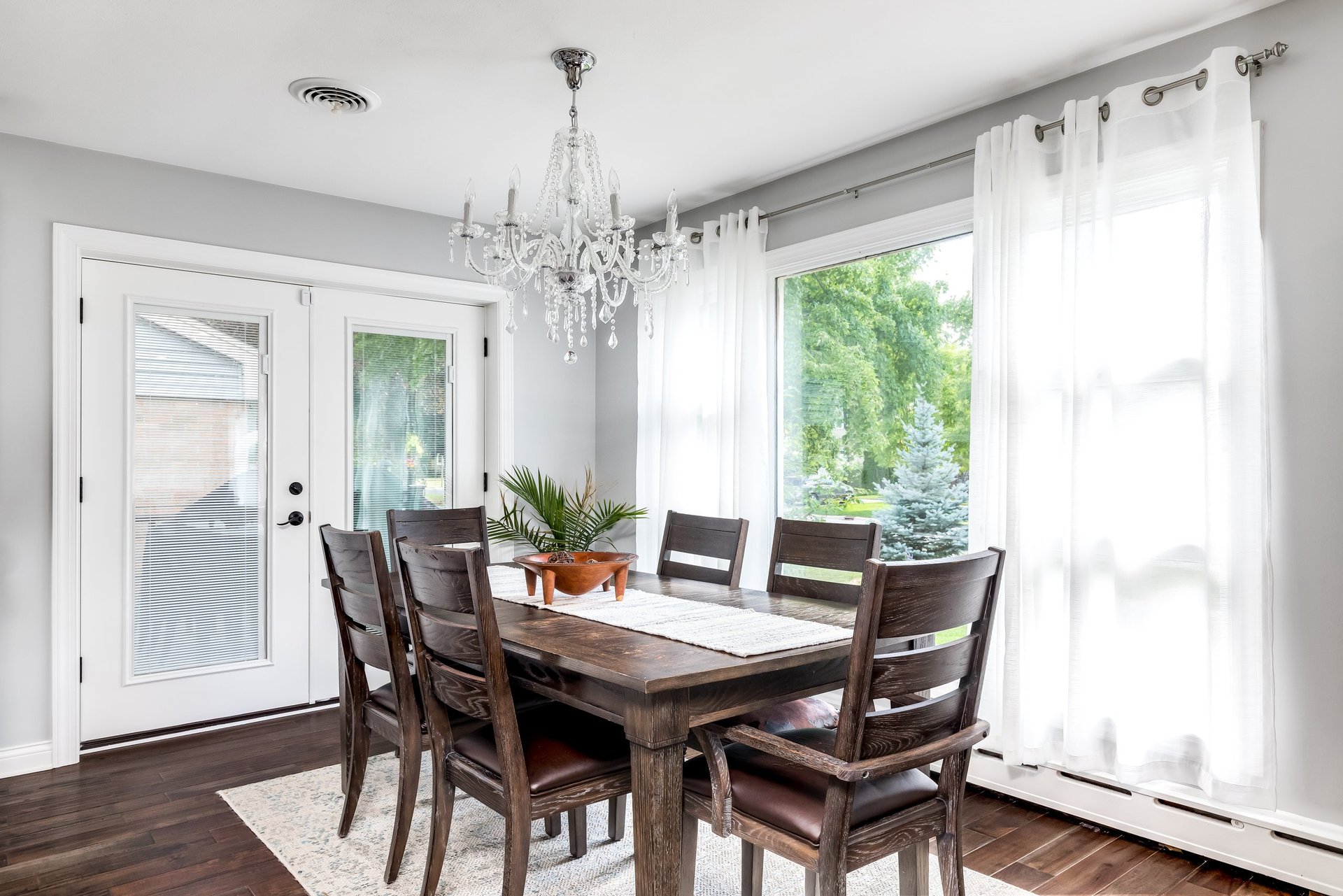 A large luxury dining room table with a grand chandelier and beautiful garden views through tall windows