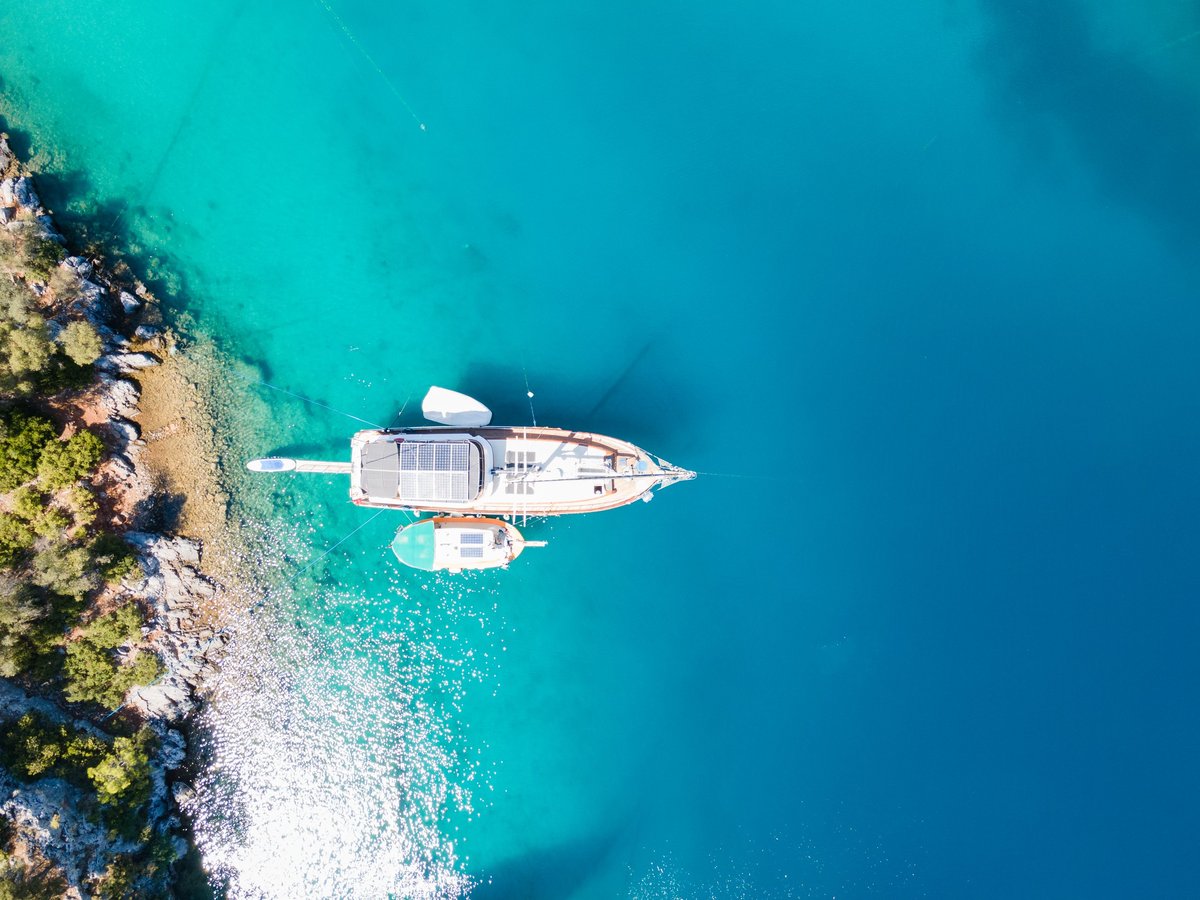 Drone photo capturing a yacht anchored in a picturesque bay in Göcek, Muğla, with its owner enjoying a relaxing swim in the turquoise waters during a blissful holiday., anchored in a calm turquoise bay at sunrise. A symbol of wealth, travel, and exclusive lifestyle in a beautiful mediterranean location