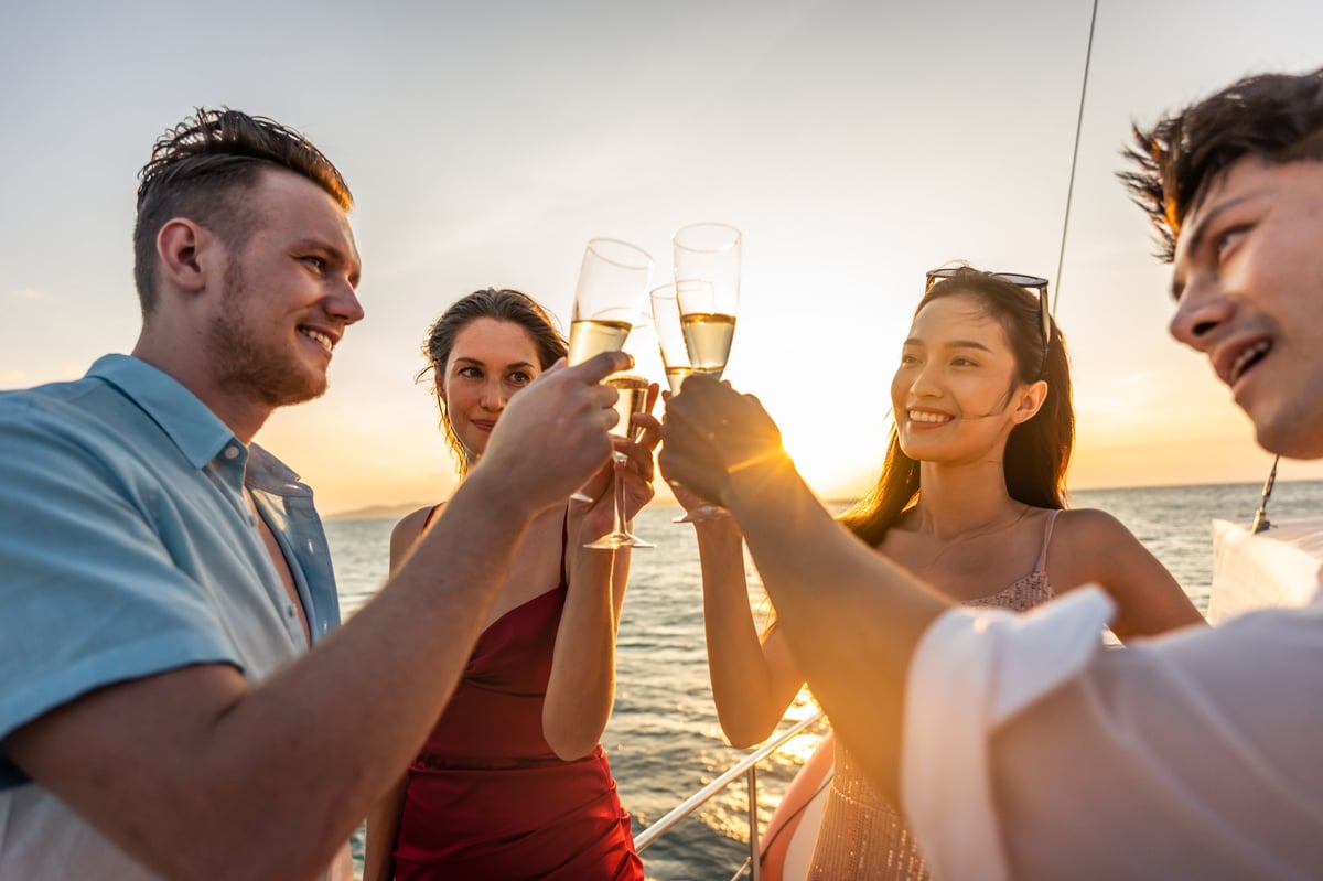 Group of diverse friends drink champagne while having a party in yacht during summer sunset