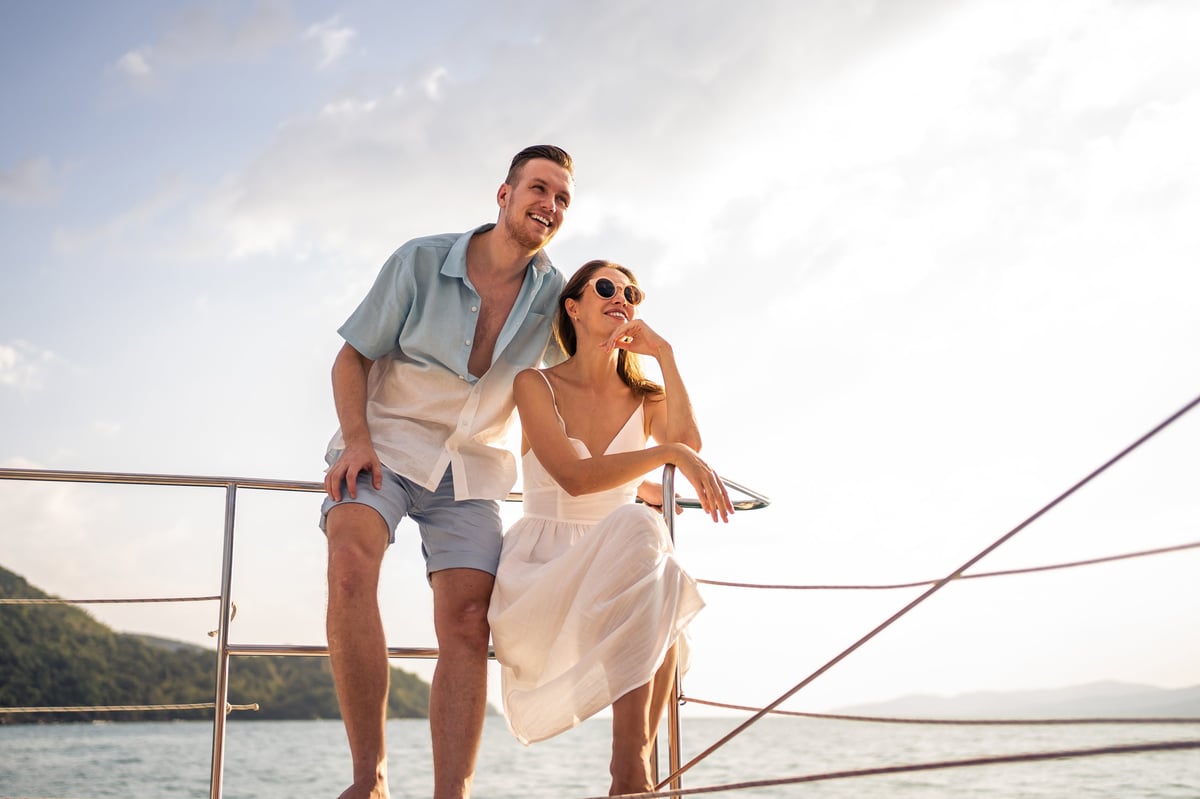 Romantic couple looking at beautiful sunset view during yacht sailing, catamaran boat celebrating anniversary honeymoon trip