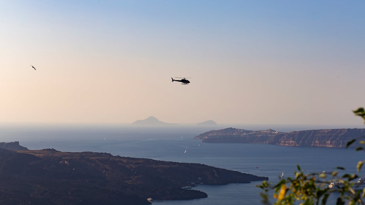 Helicopter flying over the volcanic Santorini island on a sunset sky