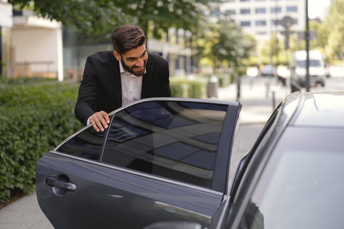 Smiling personal driver is meeting and opening car door for lady boss. High quality photo