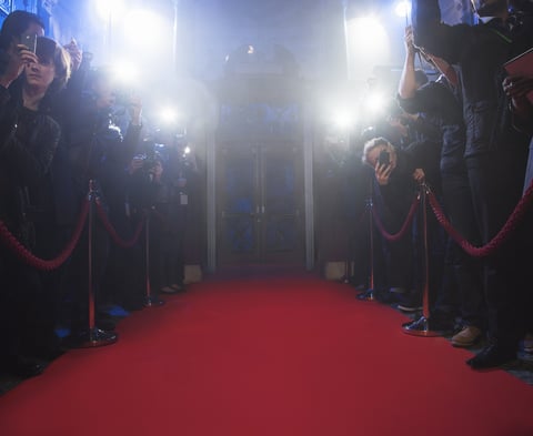 Red carpet event with photographers and flashing cameras on both sides, creating an illuminated path for arrivals.