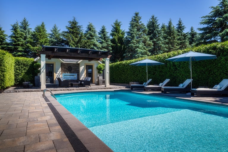 Luxury residential pool and cabana surrounded by tall hedges on a warm summer day