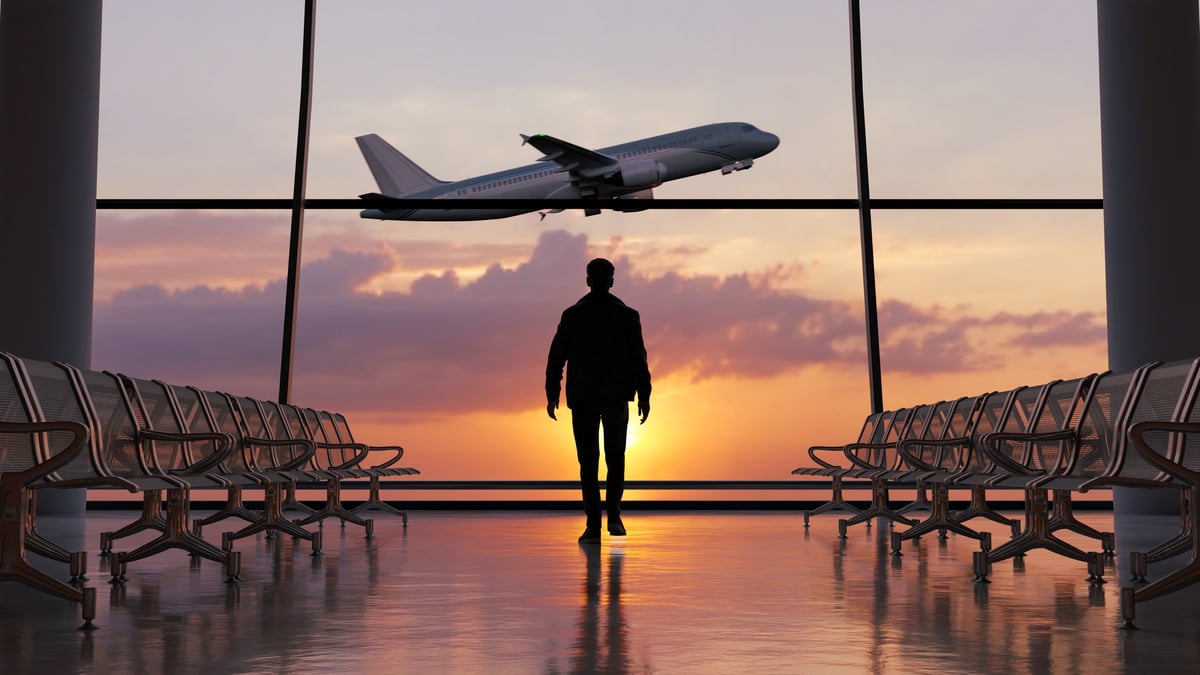 Silhouette of a man walking in the airport as the plane takes off during sunset
