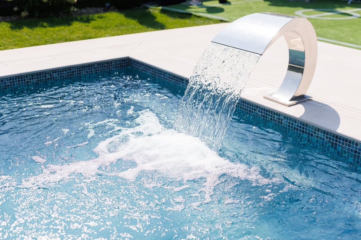 A modern swimming pool with a sleek water feature pouring water into the pool