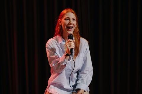Happy woman standing on stage with microphone in hand, performing stand-up comedy