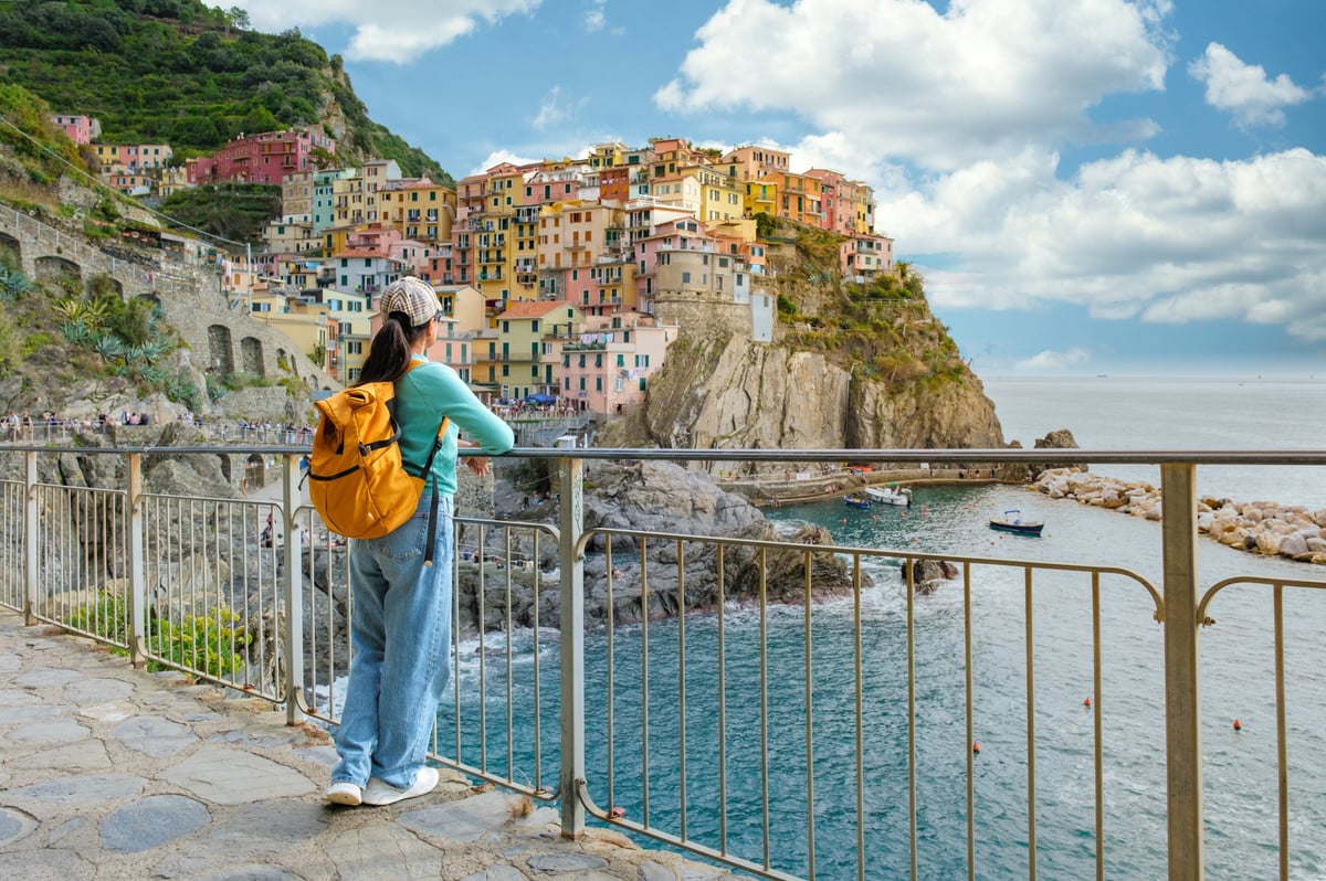 A woman wanderer stands by a railing, admiring the vibrant hues of the cliffside villages of Cinque Terre
