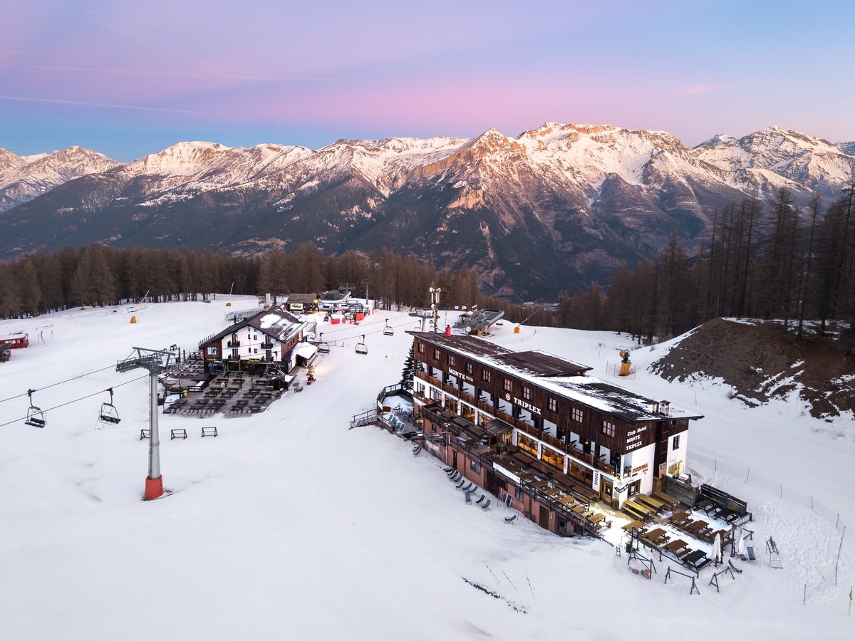 Early pink morning aerial of alpine ski resort with mountain hut and lifts