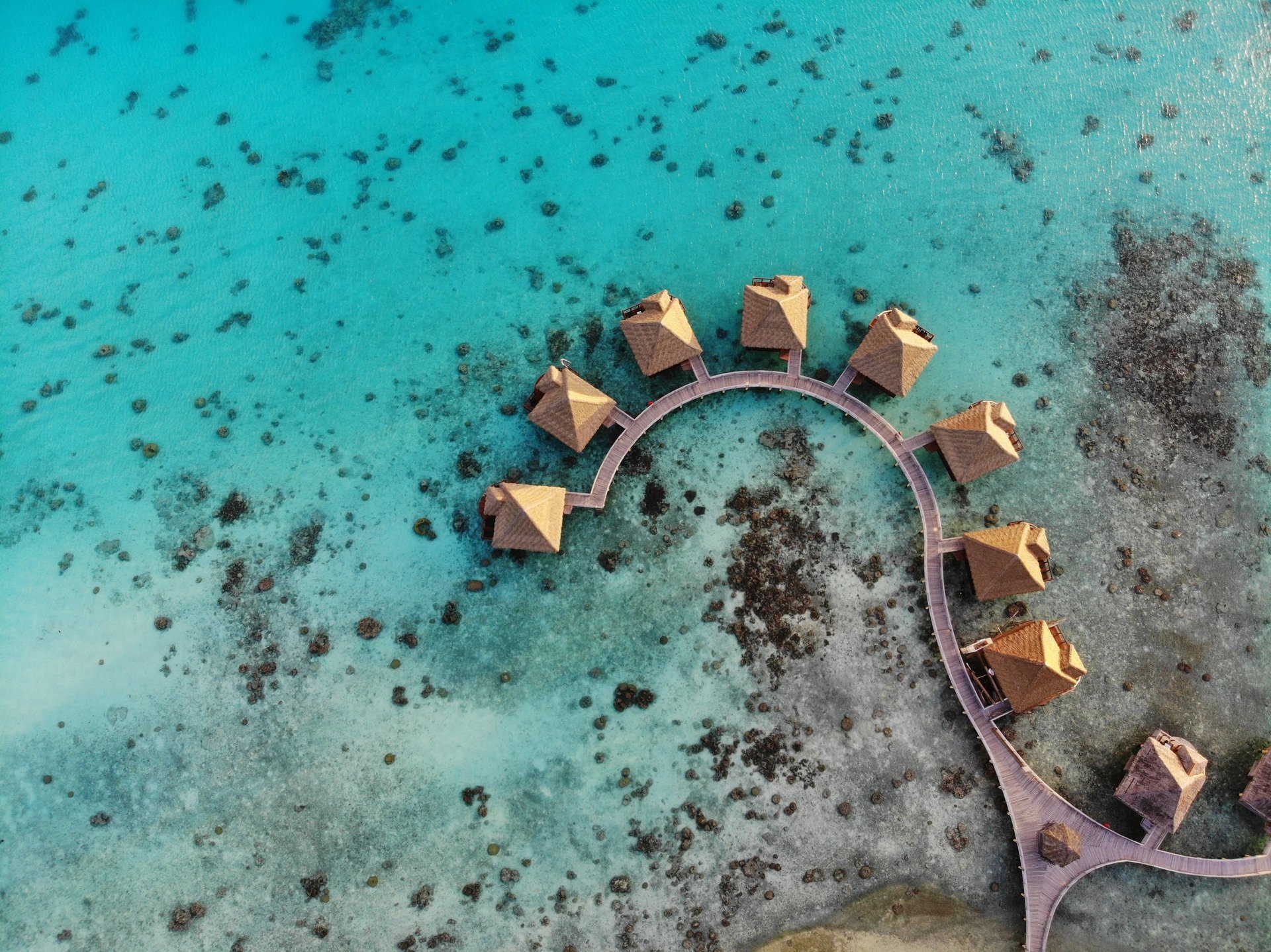 Aerial view of luxurious overwater bungalows in a serene tropical lagoon surrounded by turquoise clear water