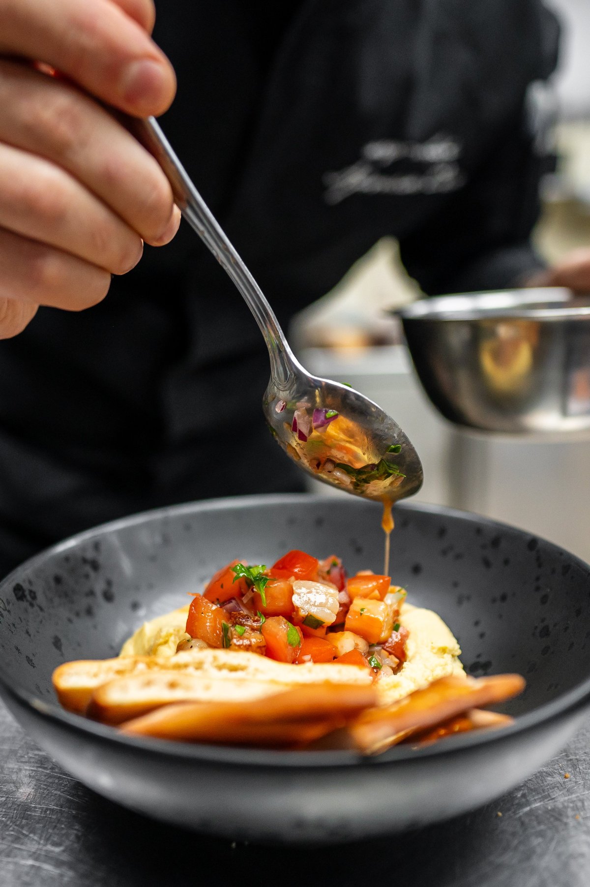 A chef skillfully plating a dish, adding a vibrant tomato topping to a smooth hummus base