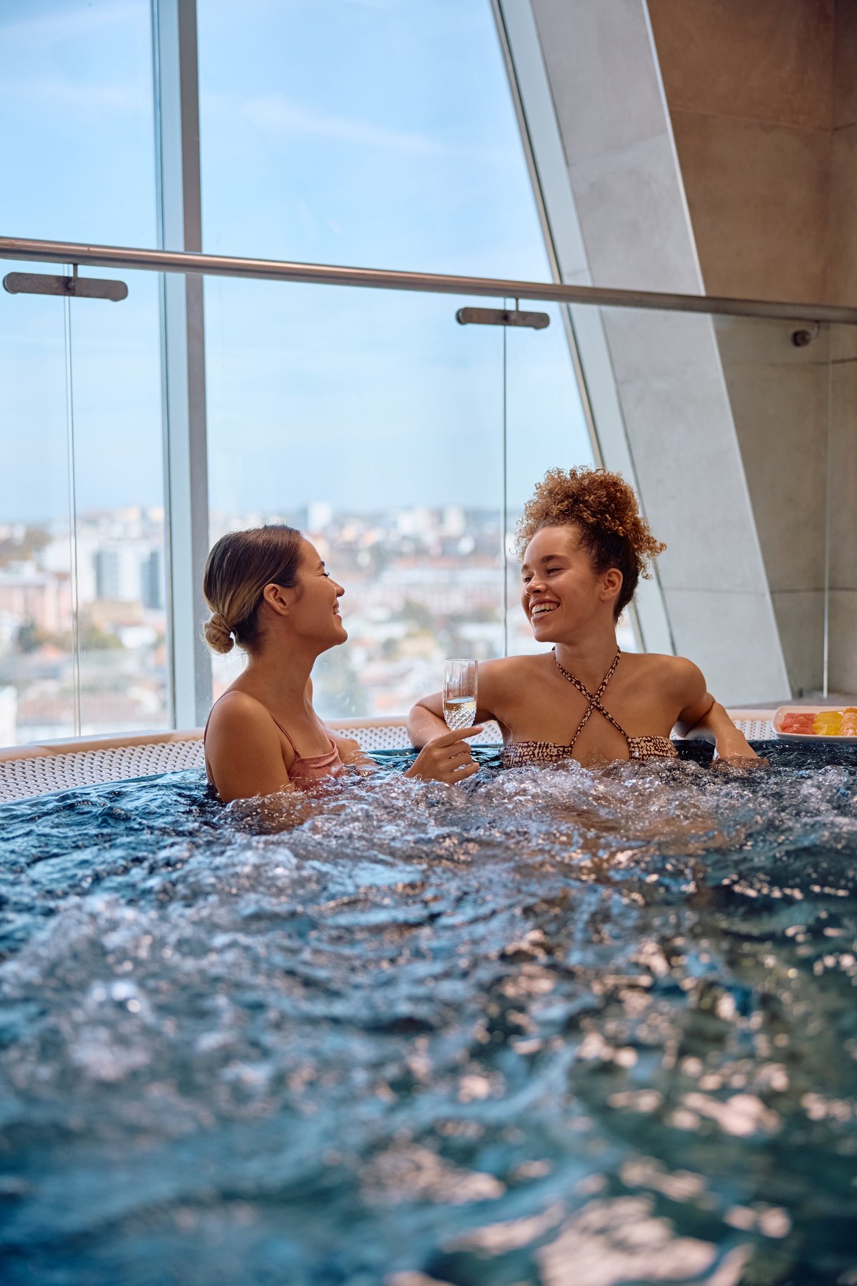 Cheerful female friends relaxing in whirlpool at wellness center
