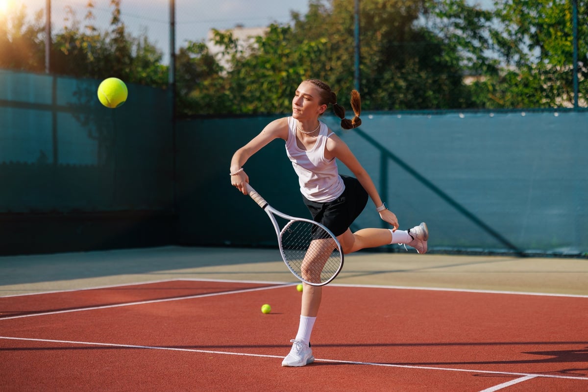 A woman tennis player demonstrates a powerful swing of her racket on the court on a sunny day