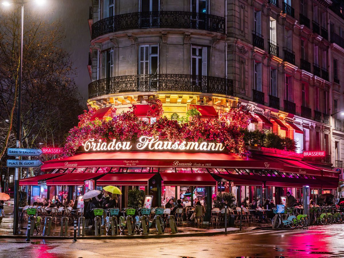 Parisian brasserie with red awnings and floral decor at dusk