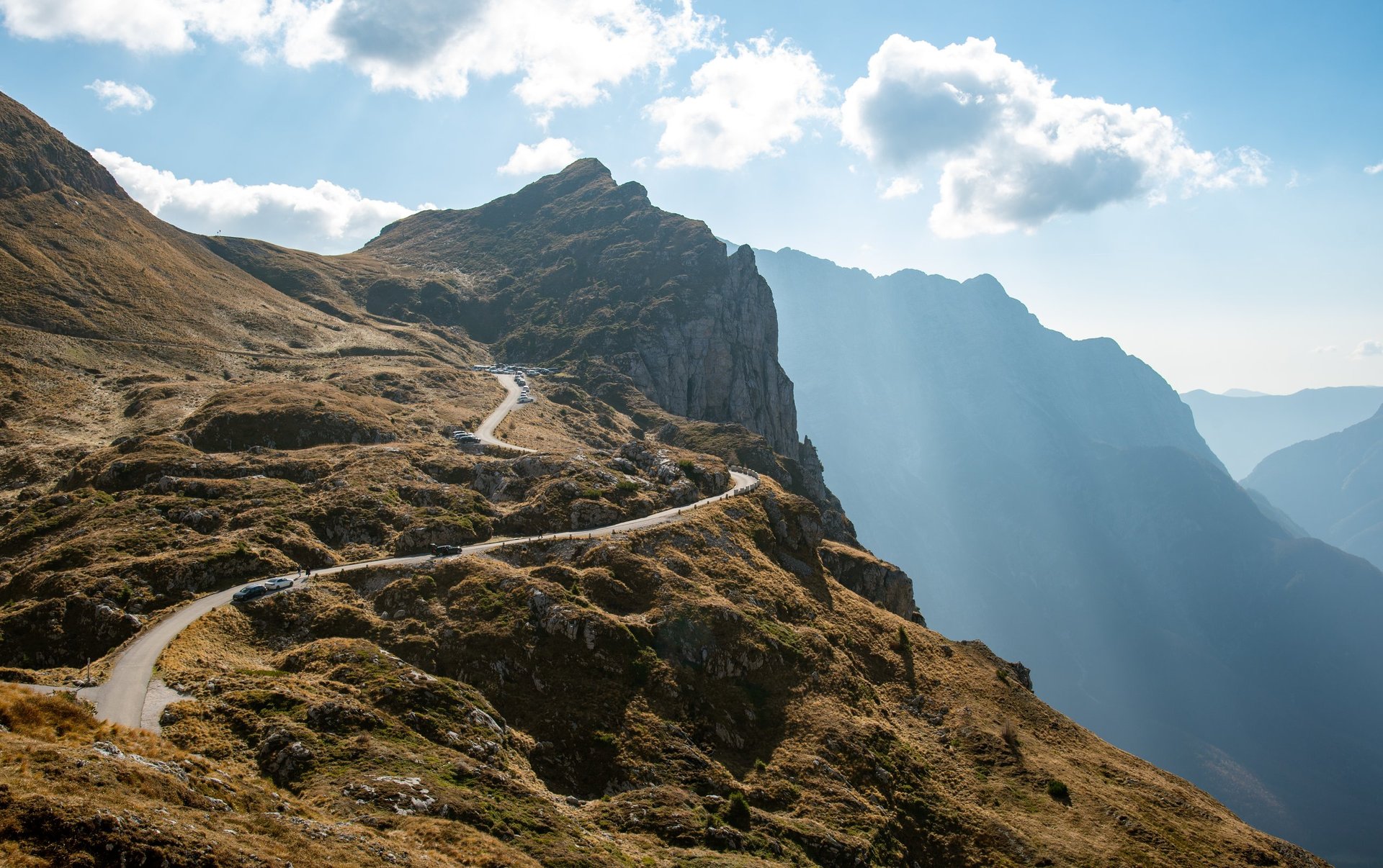 Cars traversing winding mountain road through stunning alpine scenery under bright blue sky