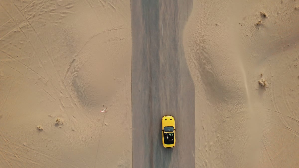 Yellow car driving through desert dunes