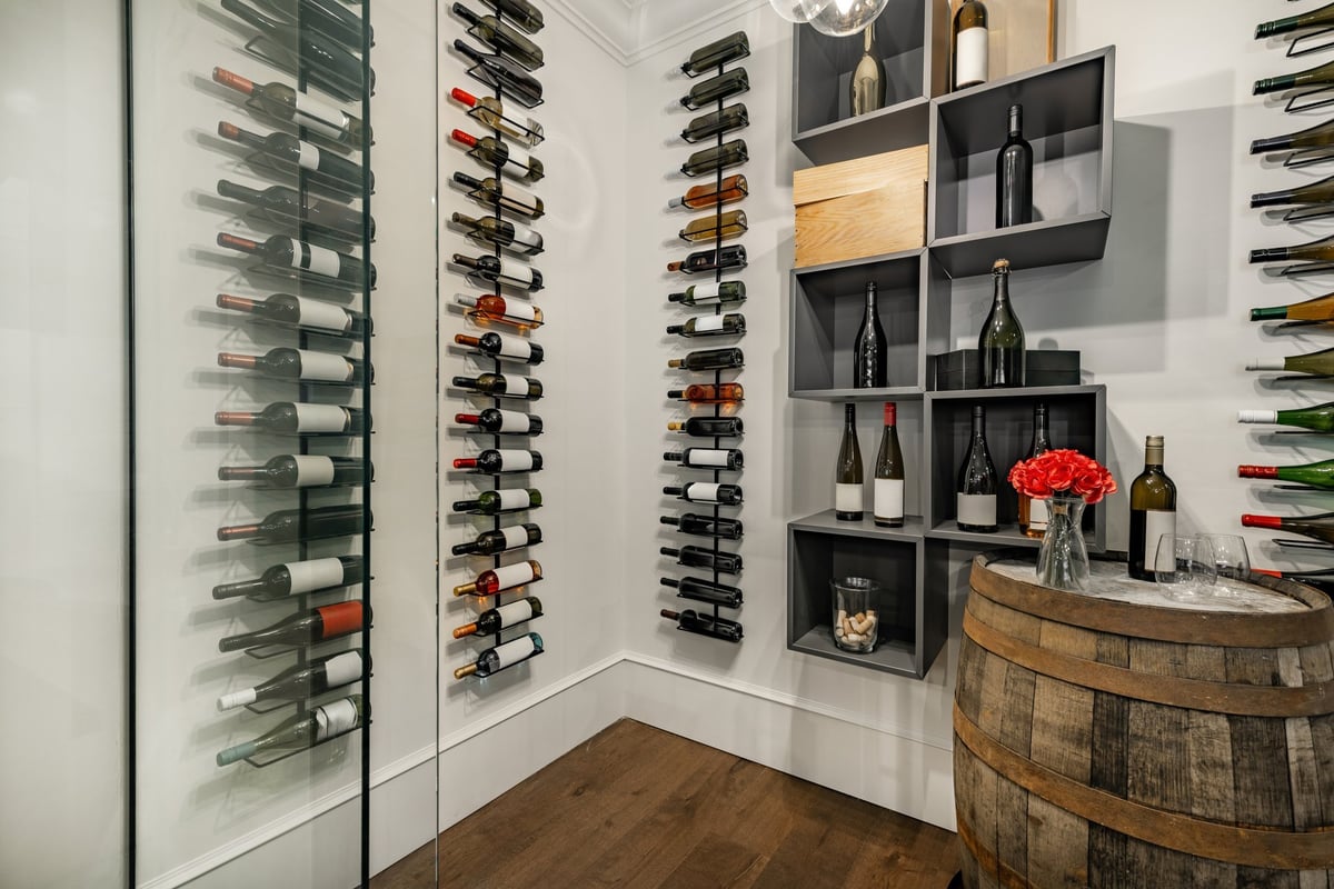 Large room of glass with hardwood floor containing multiple bottles of wine a large oak wine barrel champagne flowers built in racks and shelving full of bottles