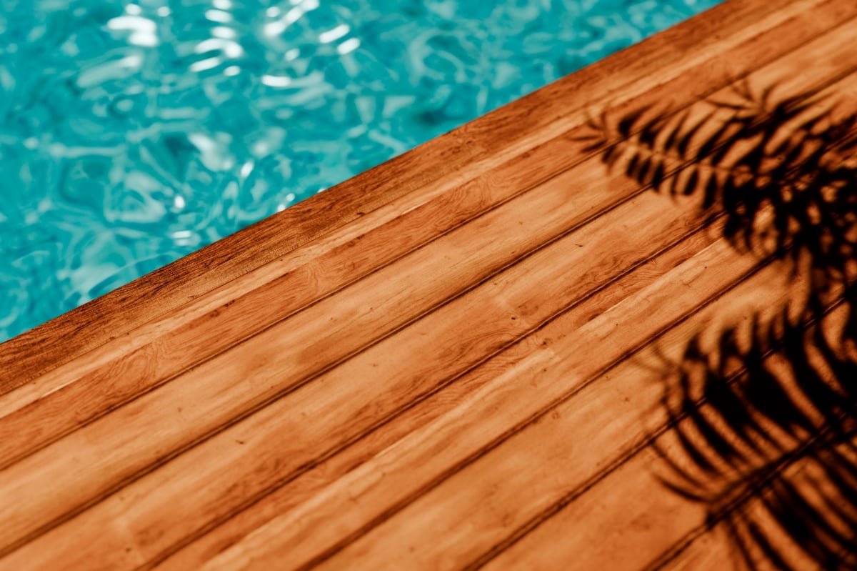 Top view of wooden decking floor with palm shadow behind luxury swimming pool