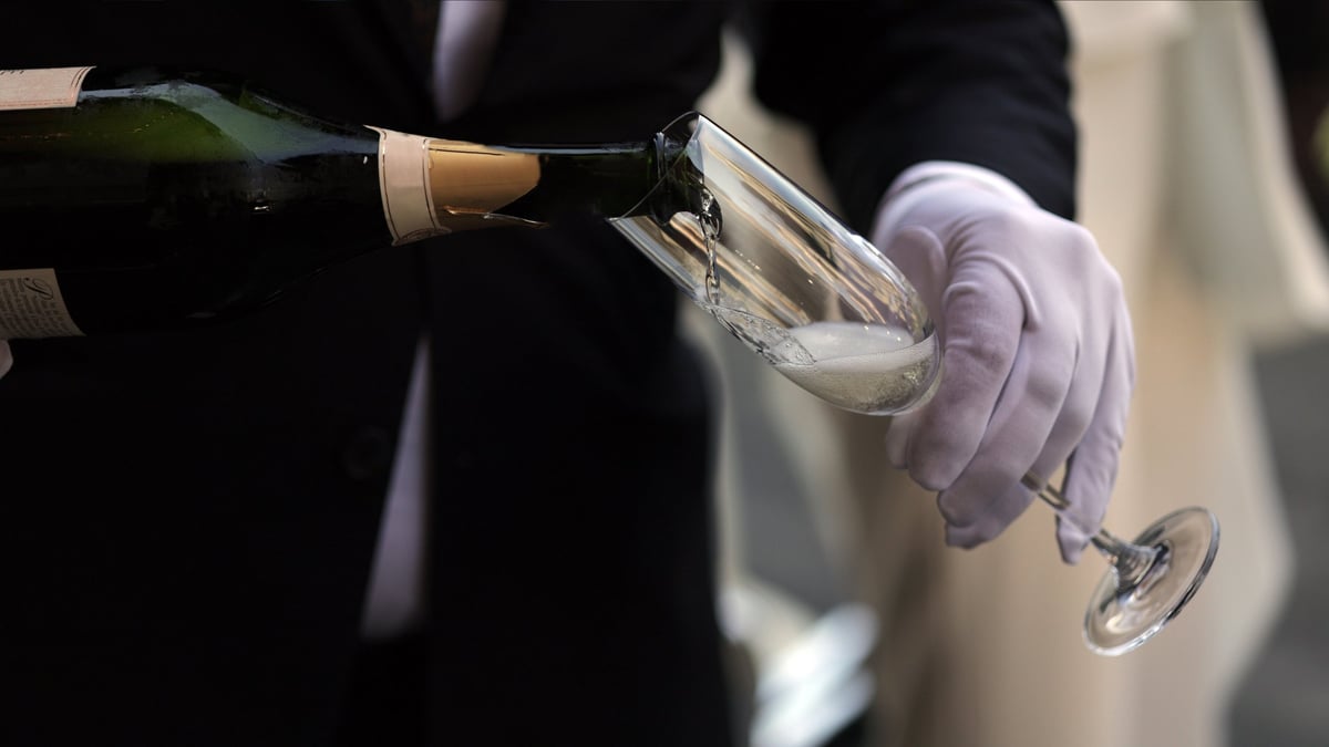 Professional server wearing white gloves pouring champagne
