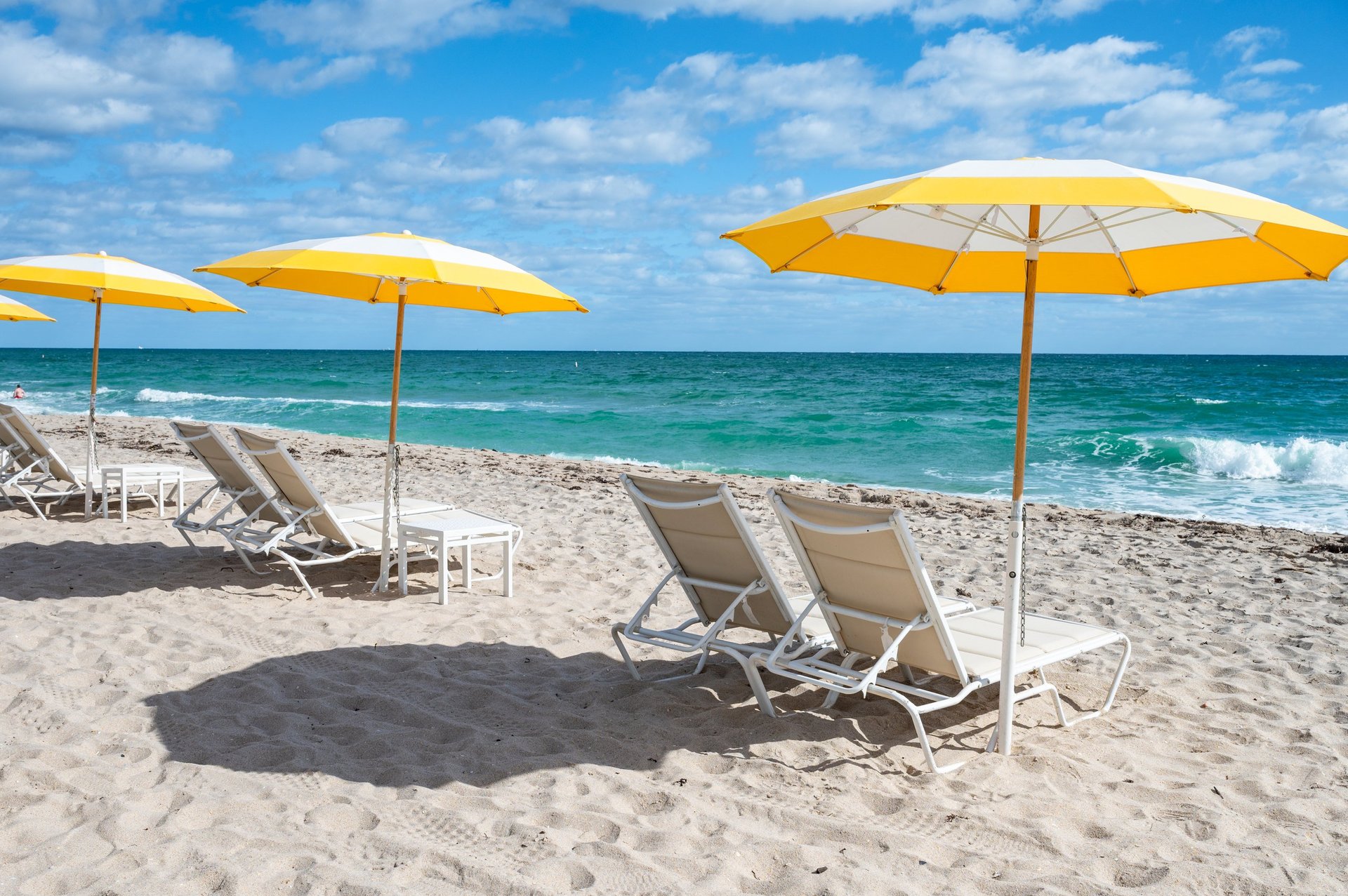Luxury beach club with yellow umbrellas and chairs on white sand by turquoise sea