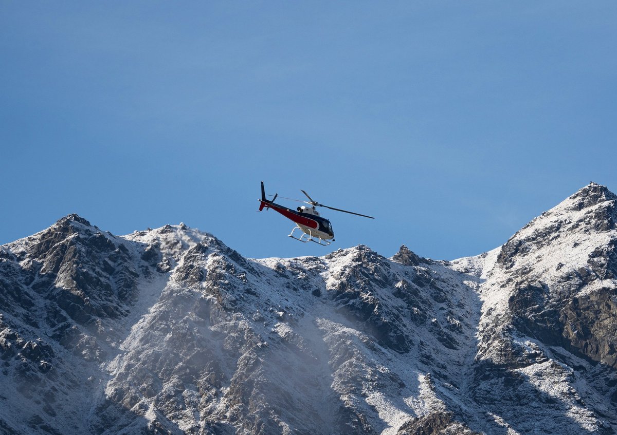 A helicopter in front of The Remarkables alpine Southern Alps mountain landscape snow covered winter wonderland near Queenstown
