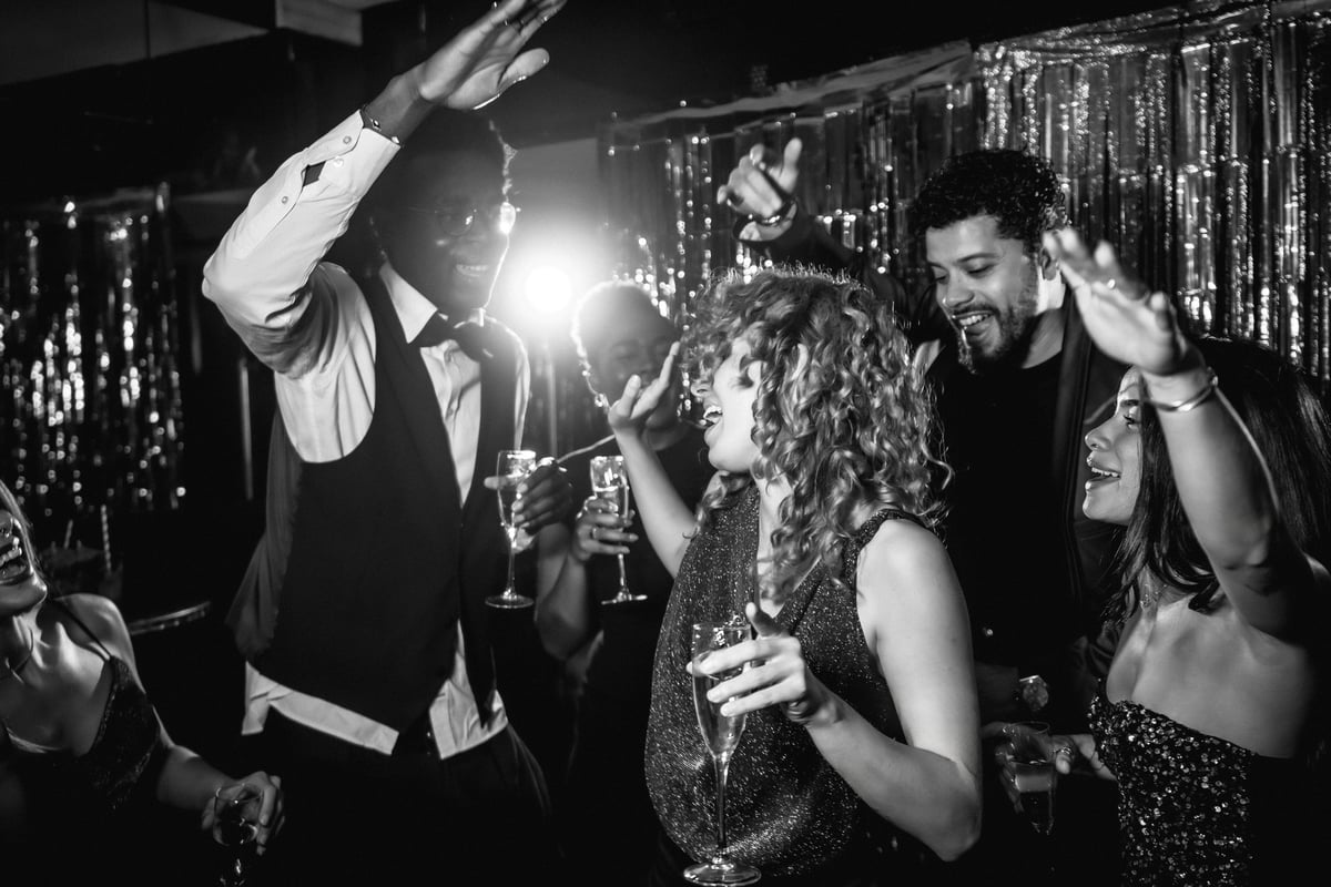 Group of stylish friends dancing joyfully and sipping champagne at a lively nightclub party