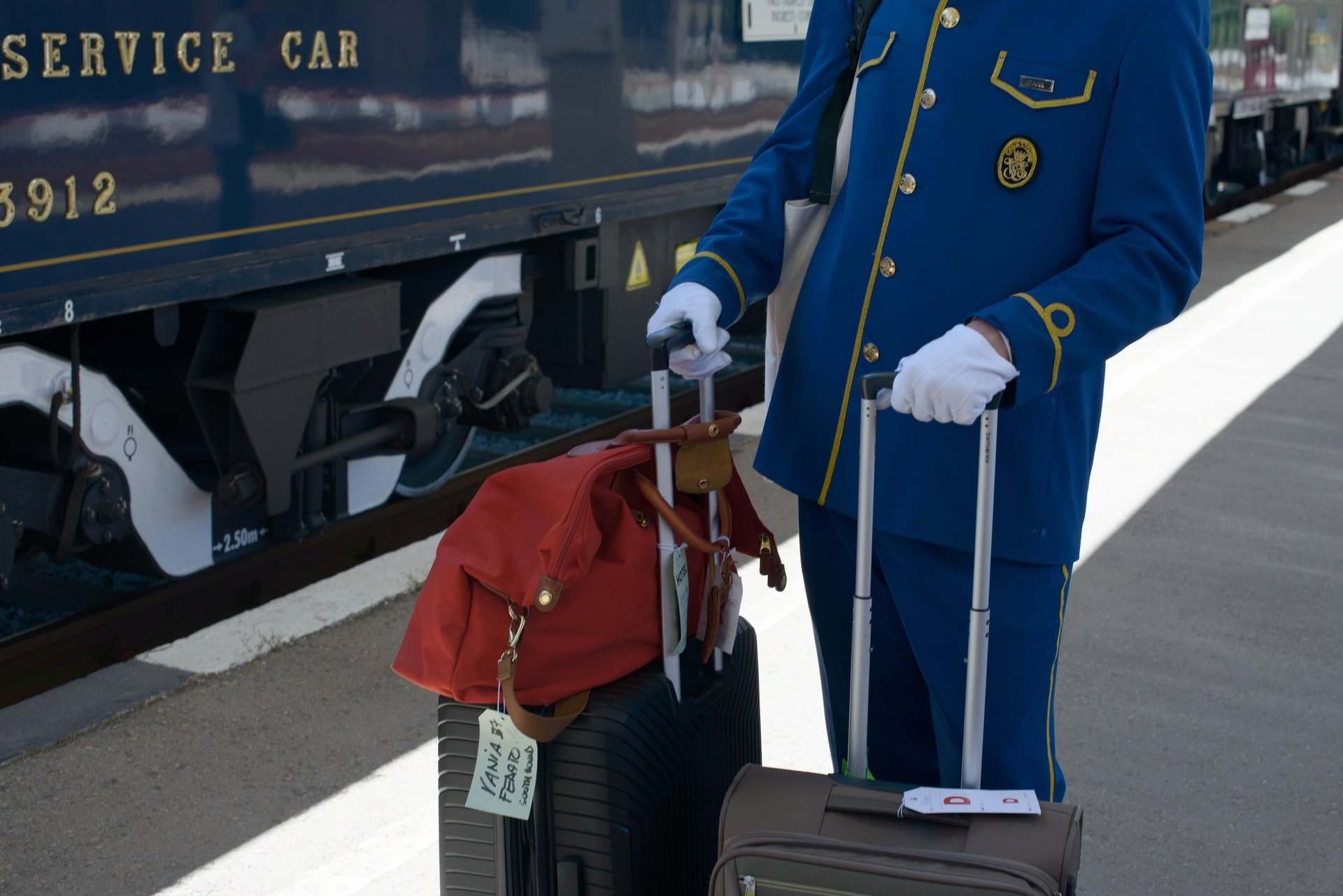 White-gloved Venice Simplon Orient Express steward in blue and gold uniform with luggage beside luxury train