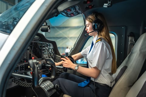 Young woman pilot using a smartphone while seated in the cockpit of a private plane