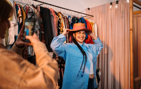 A cheerful woman beams with joy as she tries on a stylish hat inside a vibrant clothing store