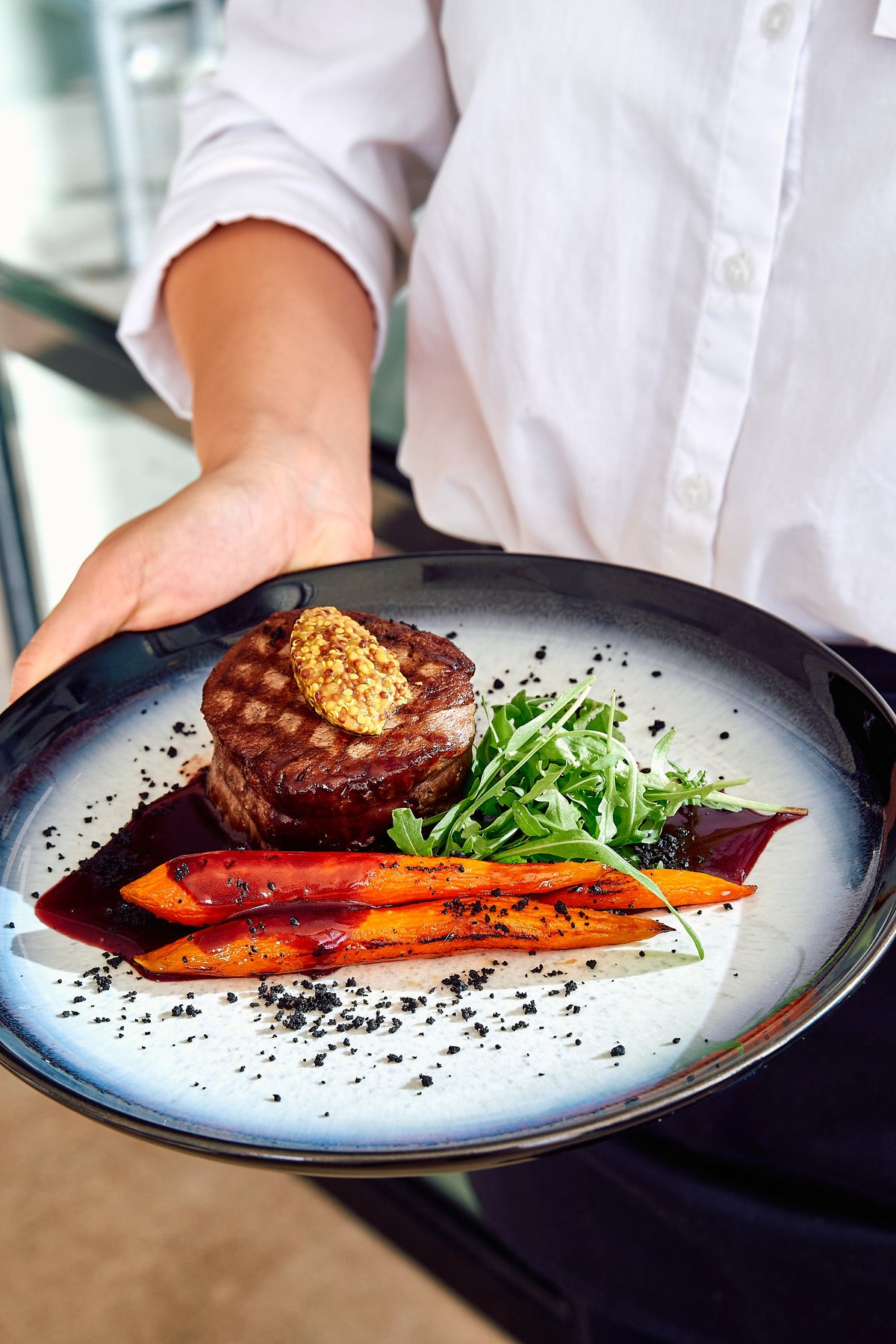 A beautifully plated gourmet steak with vegetables and sauce, garnished on a white plate