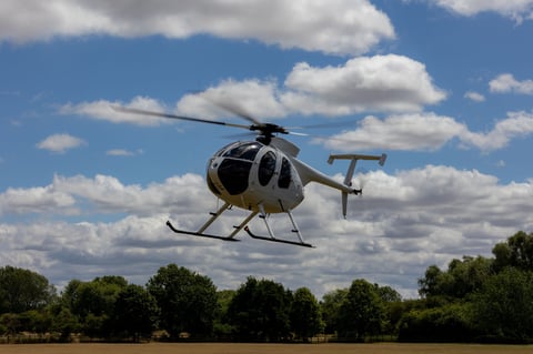 White helicopter flying over grassy field with clear blue sky