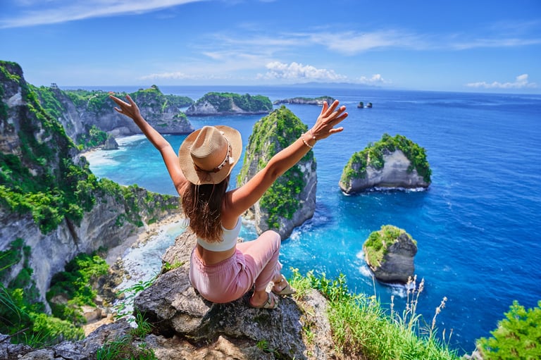 Woman traveler with open arms sitting on rock cliff and enjoying scenic landscape of Diamond beach