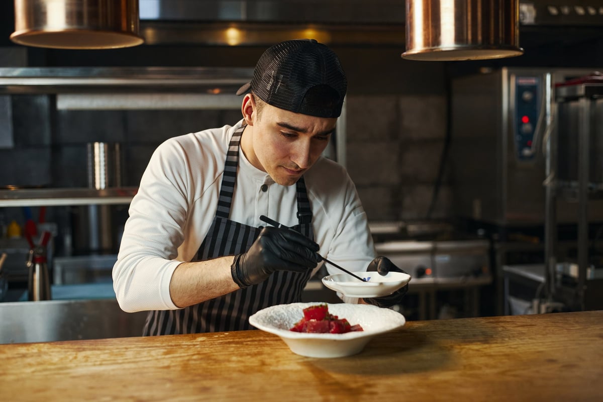 Young adult Caucasian man wearing chef uniform preparing gourmet dish in professional restaurant kitchen