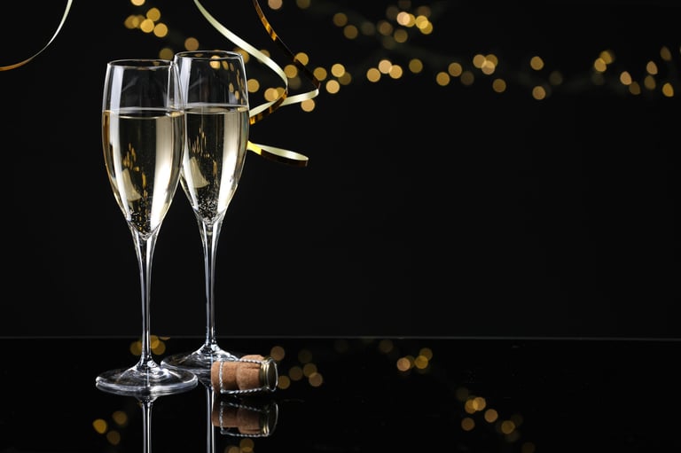 Champagne in glasses and party streamers on mirror surface against black background with blurred lights