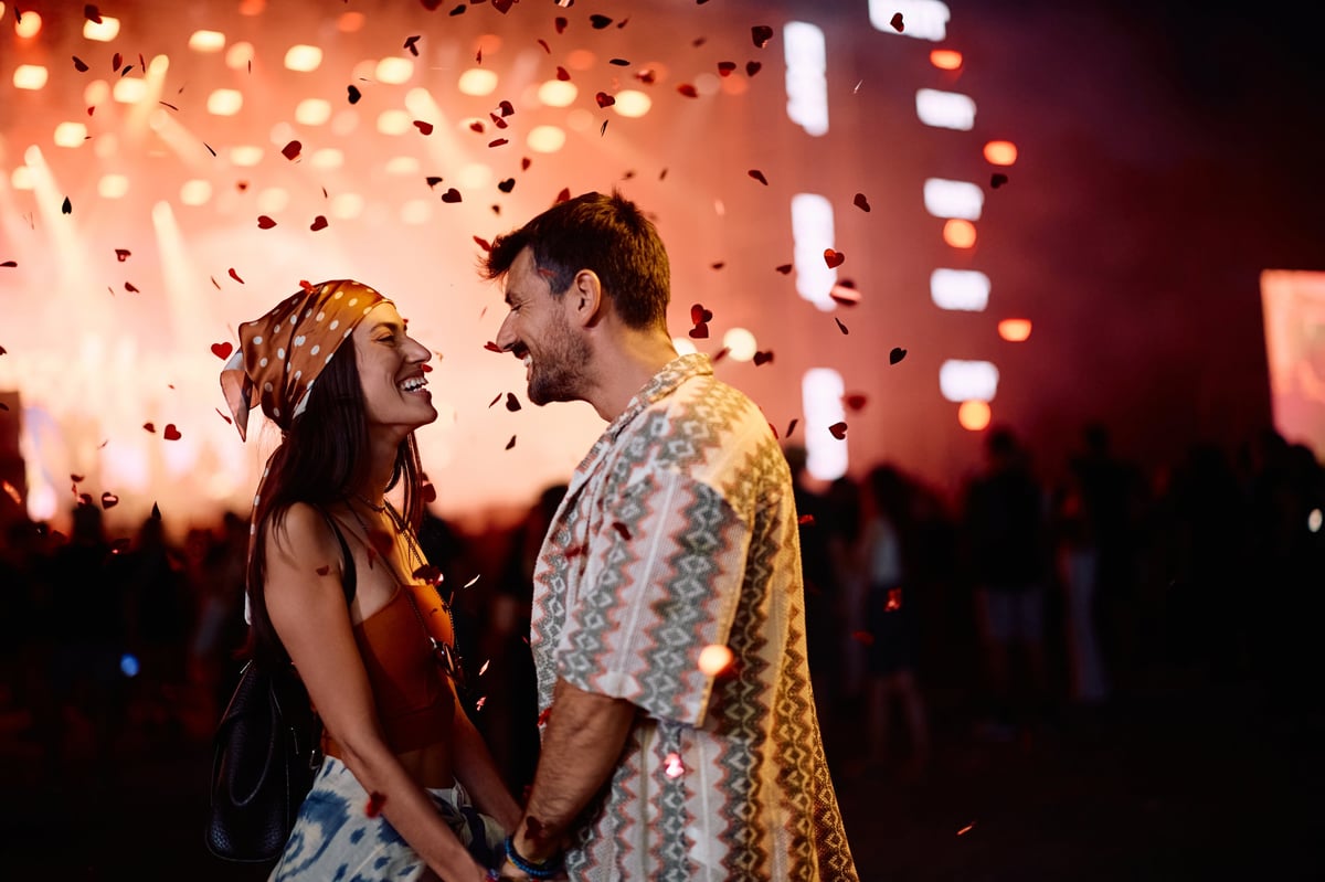 Happy couple in love holding hands under confetti fireworks at summer music festival at night. Copy space.