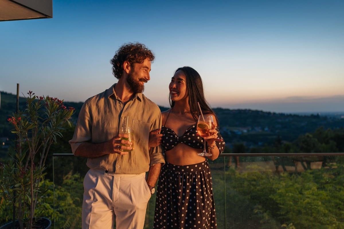 Happy couple on balcony with drinks enjoying sunset over landscape