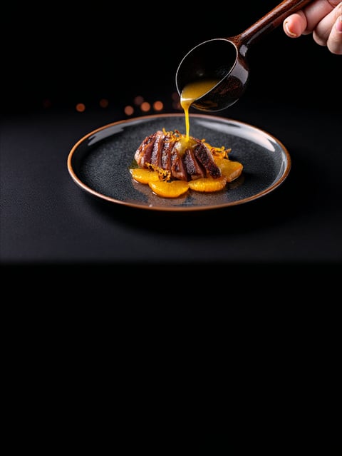 Sliced duck breast with orange sauce being served on a dark gray plate at fine dining restaurant