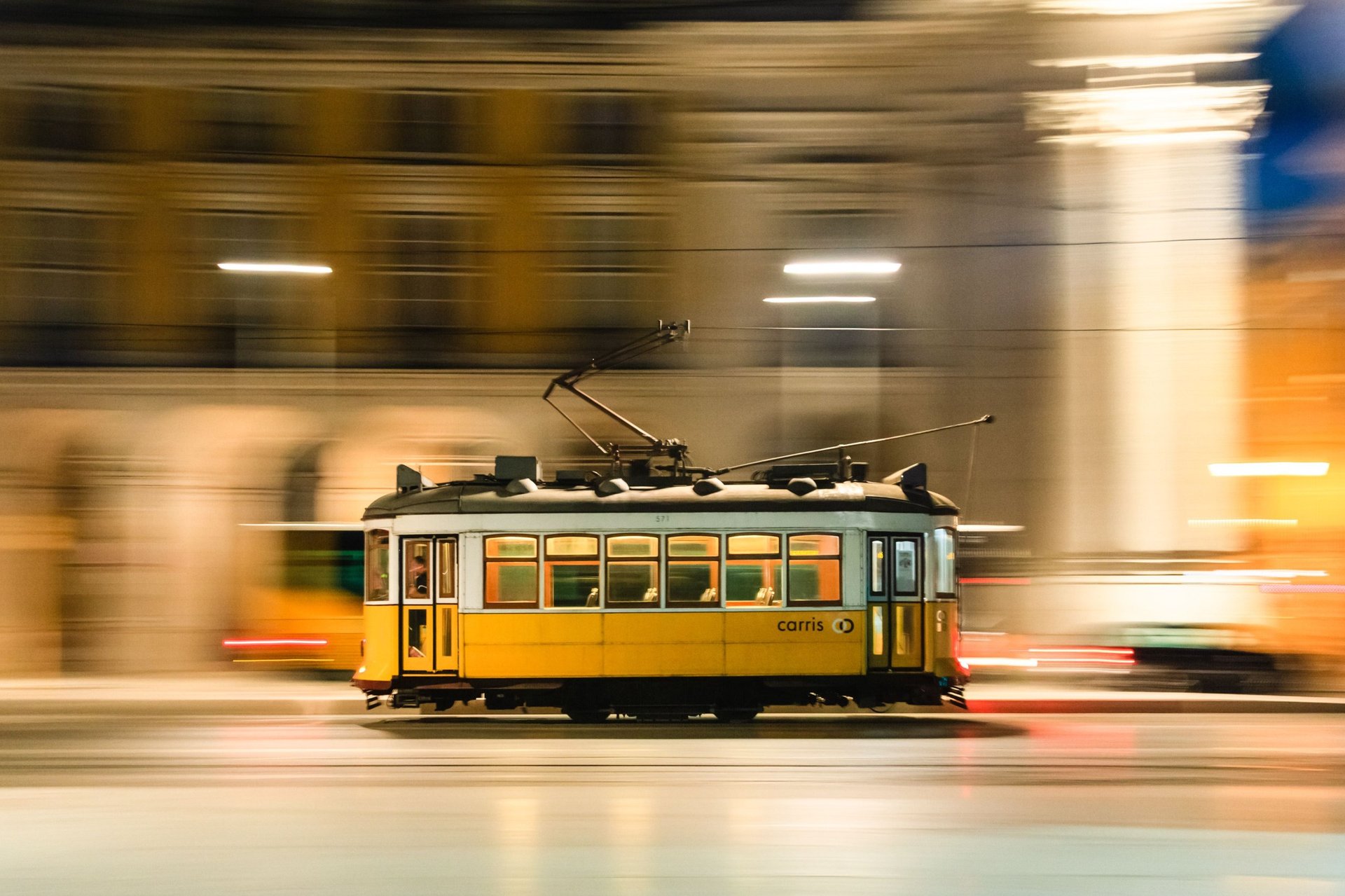A vintage yellow tram in motion through Lisbon's cityscape at night, capturing urban transit energy