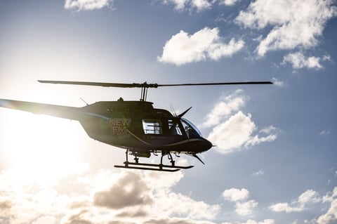 Silhouette of helicopter flying against bright sky with clouds