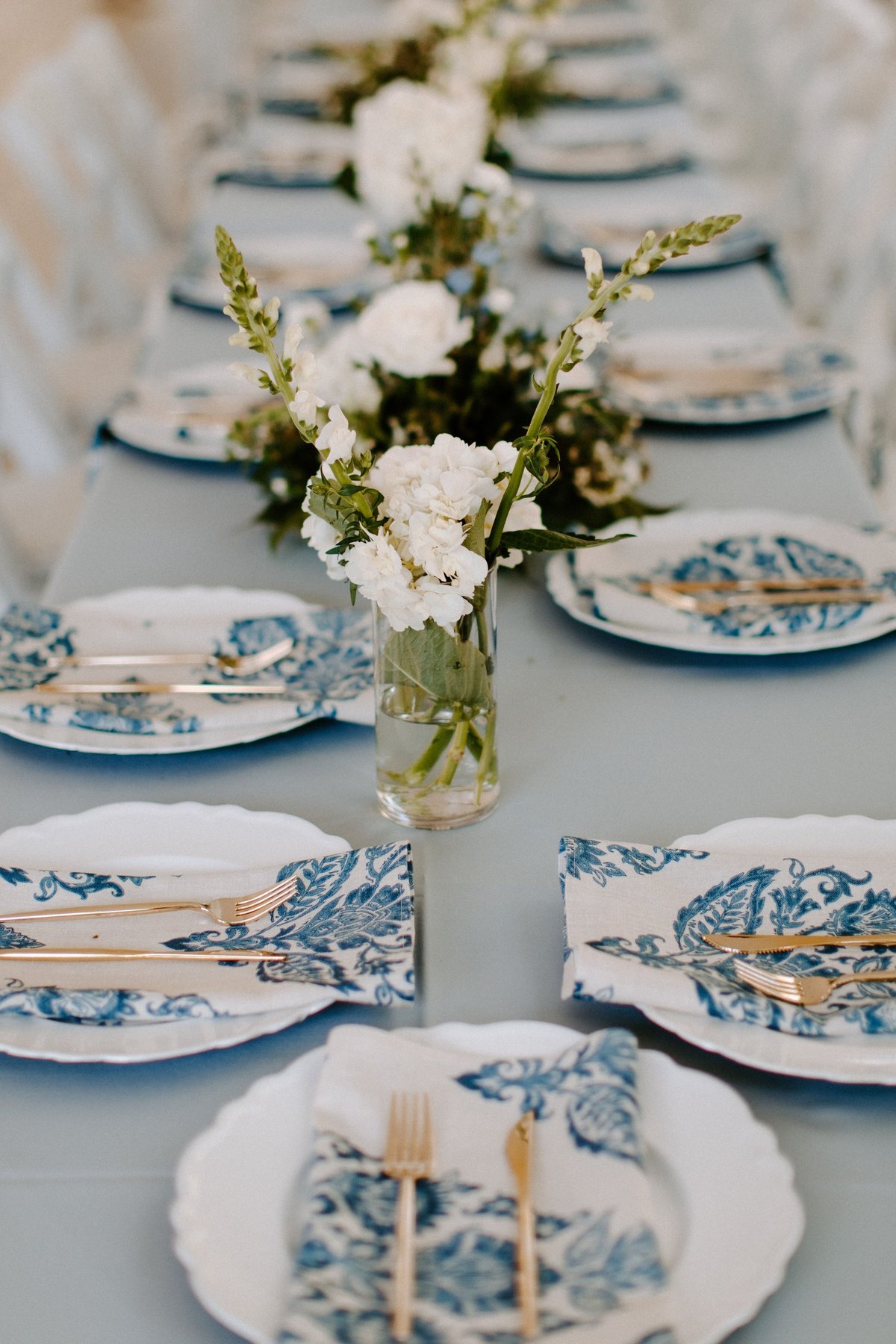 Elegant wedding table setting with blue patterned plates, gold flatware, crystal glasses and floral centerpieces