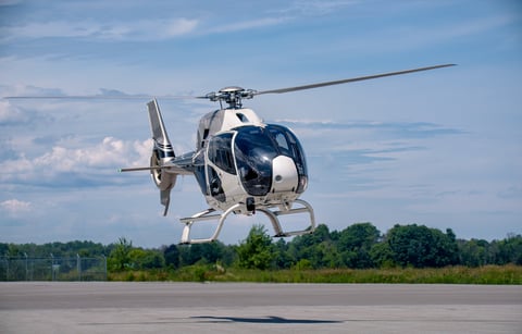 A white Airbus H120 helicopter is captured in a low hover above the runway