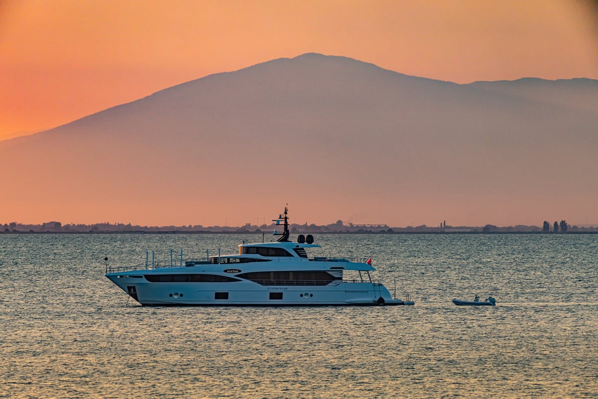 Luxury motor yacht anchored at sunset in the Mediterranean with mountains in the background
