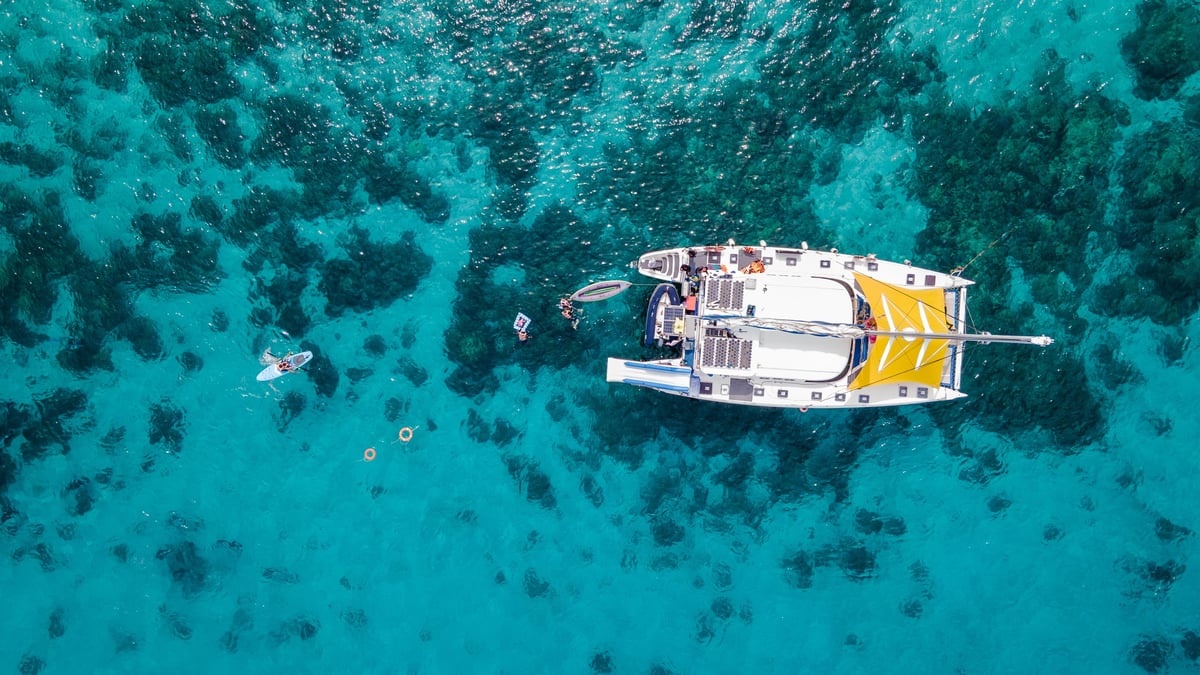 Aerial top view of sailing catamaran anchor over turquoise water