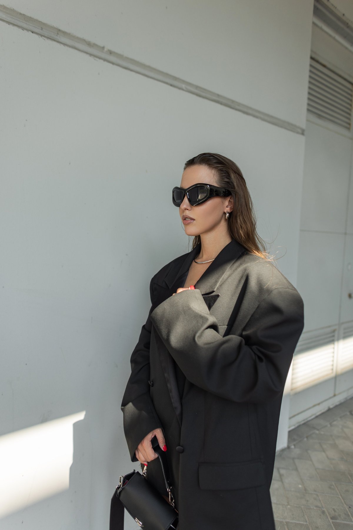 Stylish young woman in oversized black blazer and sunglasses posing outdoors, close-up fashion portrait with modern urban vibe and confident look.