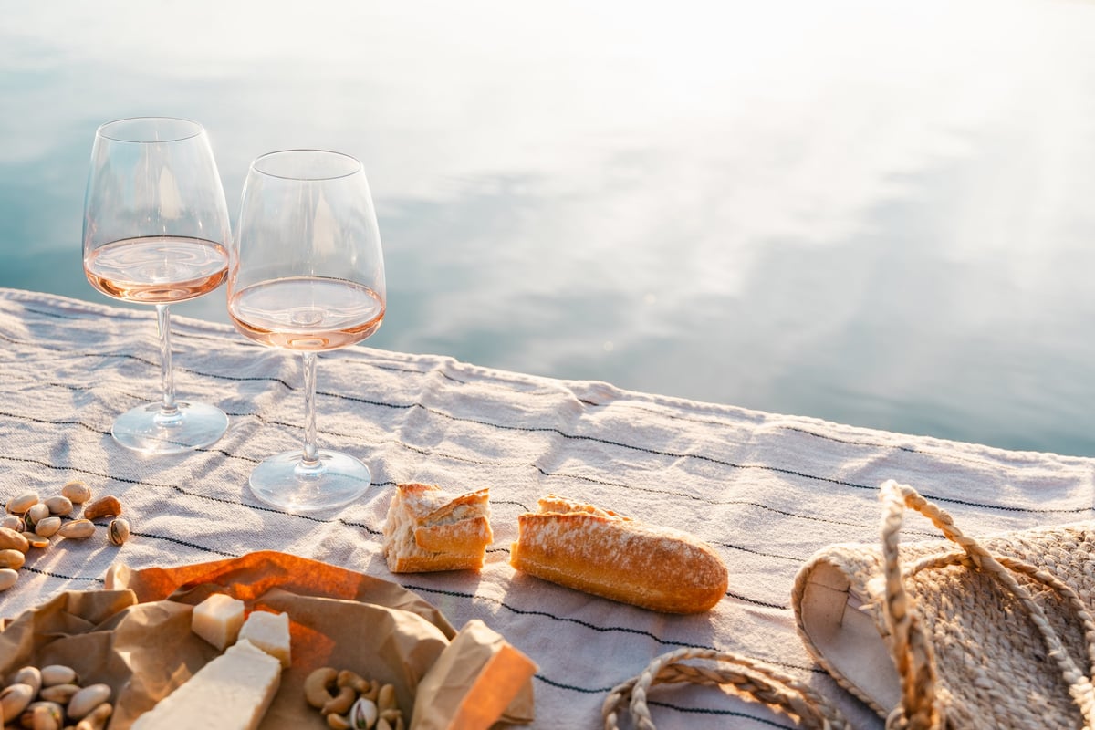 Two glasses of rose wine with cheese and nuts on a pier at sunset